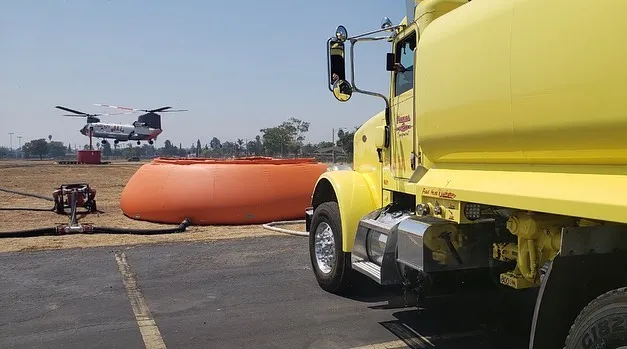Yellow semi truck parked in front of a large orange water tank.