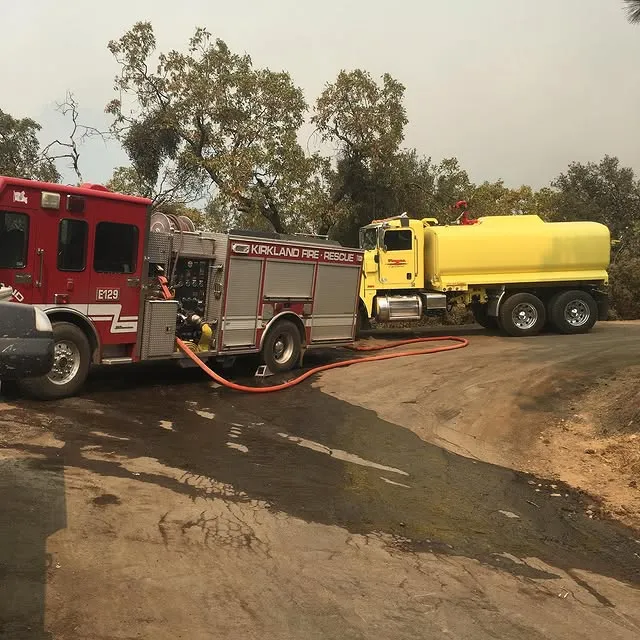 Yellow semi truck parked behind a red fire truck.