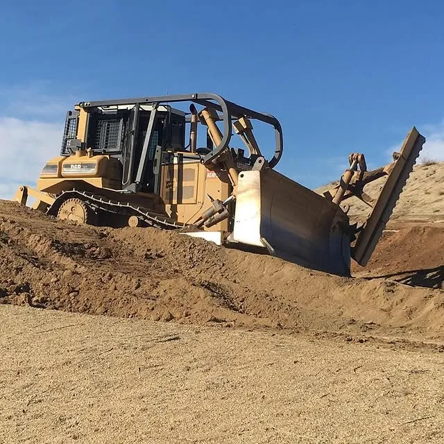 A large yellow bulldozer digs into a pile of dirt, its front and back wheels, legs, arms, and buckets visible.